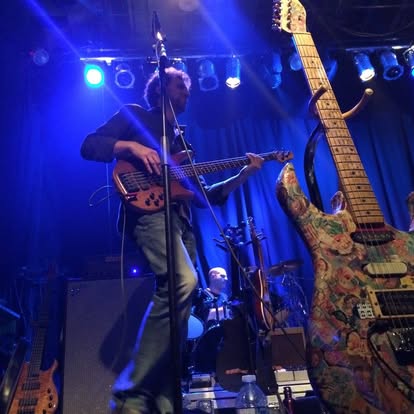 B. Jay Nathan performing live on stage playing a 5-string bass guitar under blue stage lights